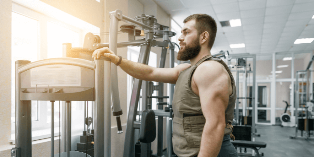 Man bär viktväst och tränar på gymmet vid en träningsmaskin.